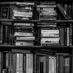 A black and white image of a packed bookshelf with various books in a library setting.